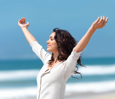 Pretty young woman with arms raised standing on beach